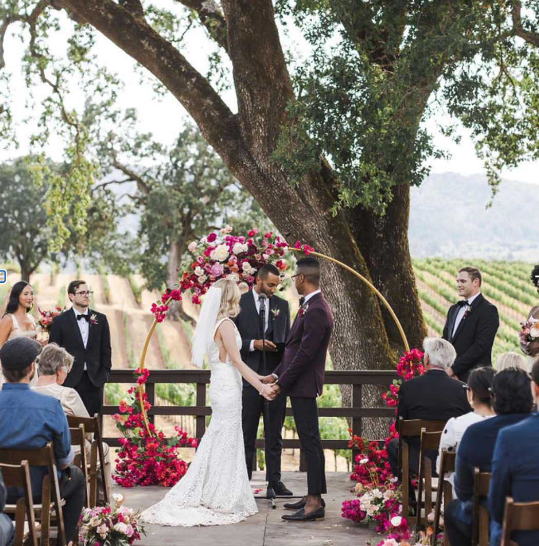 Ceremony at the amphitheater with a floral arch and vineyard backdrop