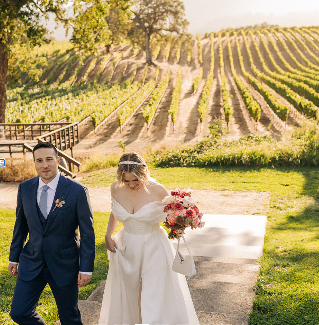 Newlyweds walking beside the amphitheater with vineyard rows in the background
